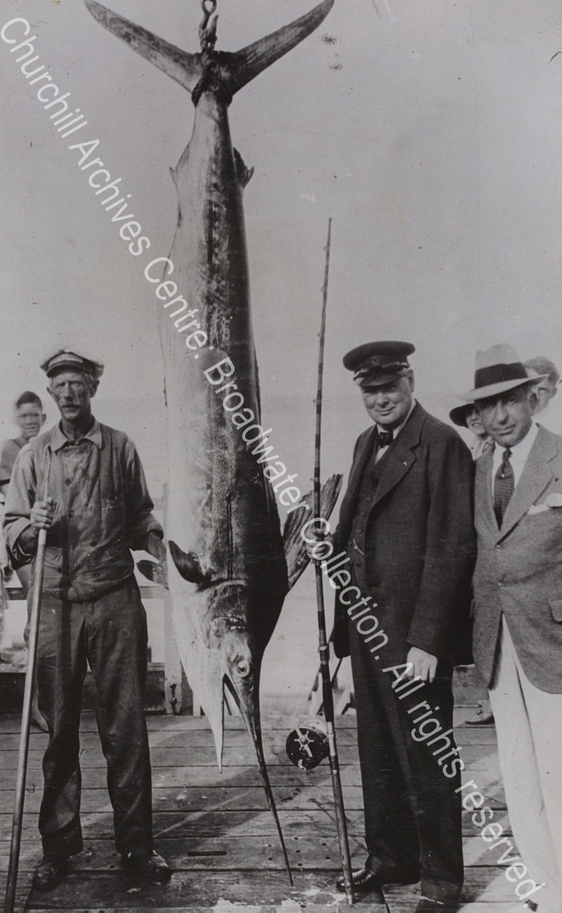 Photo shows WSC wearing a cap and carrying a fishing rod standing next to a huge fish.
