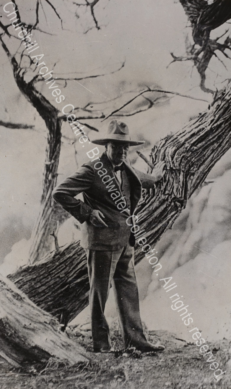 Photo of WSC leaning against a large tree wearing a wide-brimmed stetson hat.