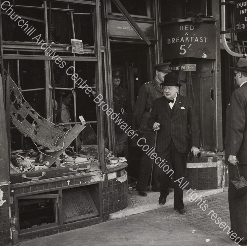 WSC is shown walking out of a bomb-damaged building. A sign behind him reads "Bed & Breakfast 5/".