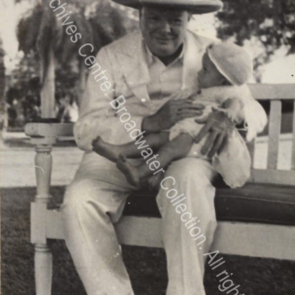Photo shows WSC smiling and sitting on a bench with a baby [?Victor Lampson