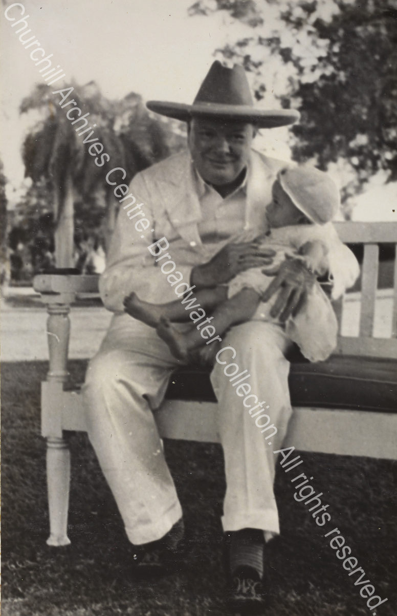 Photo shows WSC smiling and sitting on a bench with a baby [?Victor Lampson