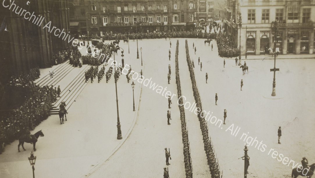 Aerial photograph of two long lines of troops drawn up outside a large building [? Cologne cathedral] in Germany