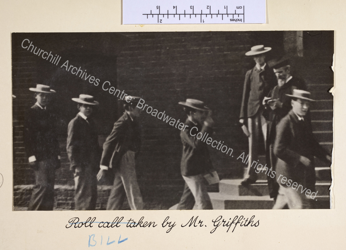 Photograph shows Harrow schoolboys wearing straw boaters filing past a school master wearing a gown and mortar board. Note that caption originally read "Roll call taken by" and has been corrected.