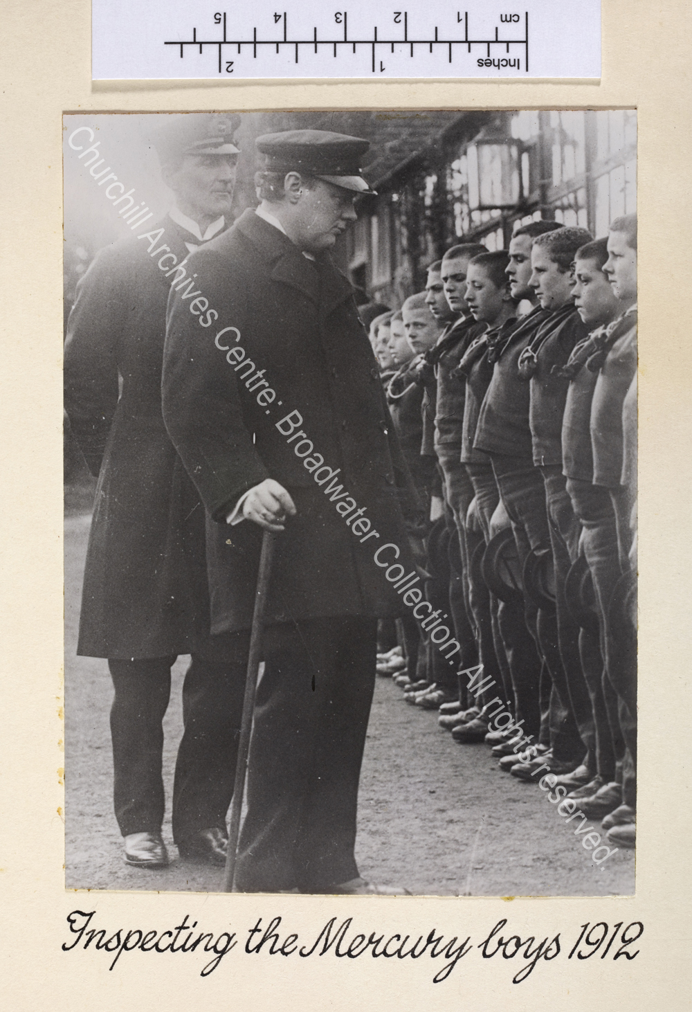 Photo shows WSC walking along a line of boys who are standing to attention and wearing uniform.