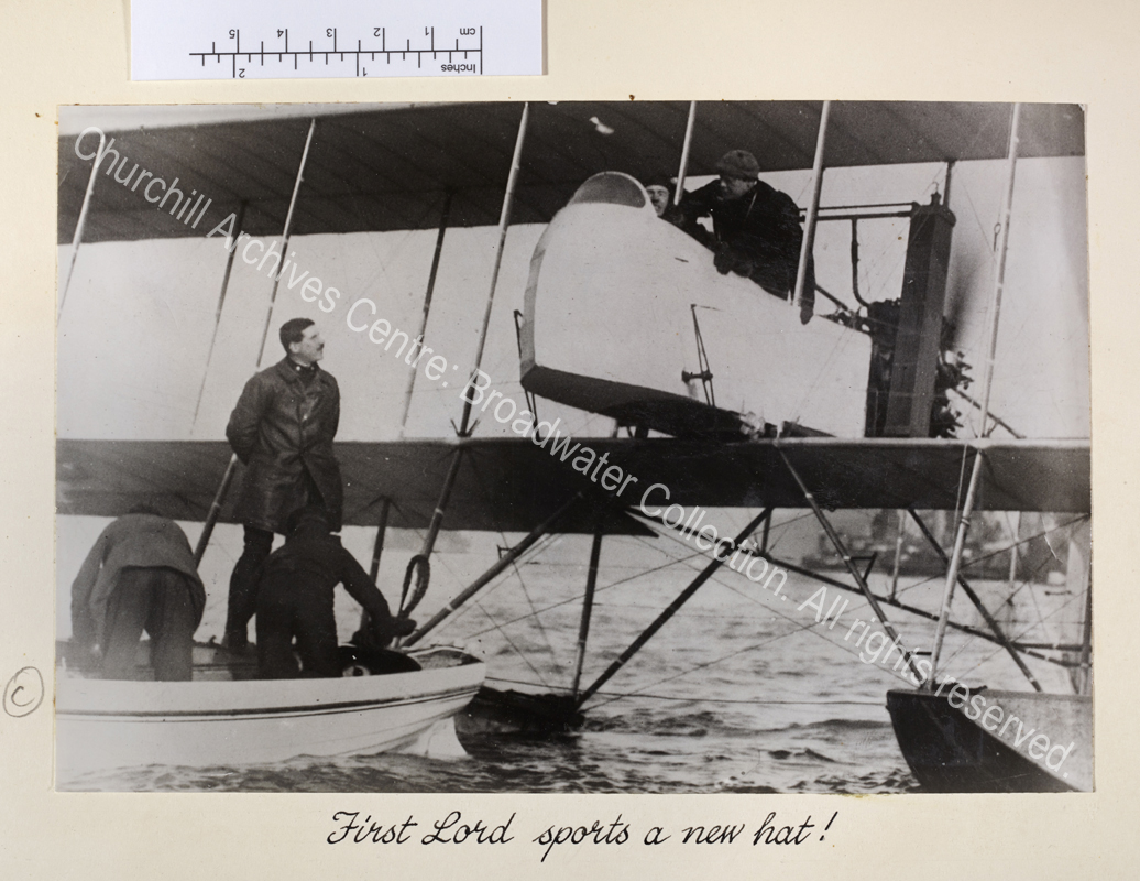 Photo shows WSC in the cockpit of a seaplane and a small boat on the water beneath the plane.