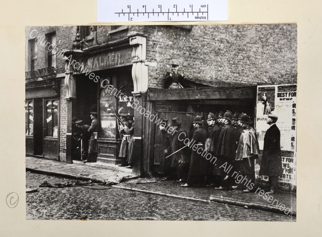 Photo taken during the siege showing armed soldiers and Metropolitan policemen sheltering in doorways. WSC and Edward Marsh are with the police