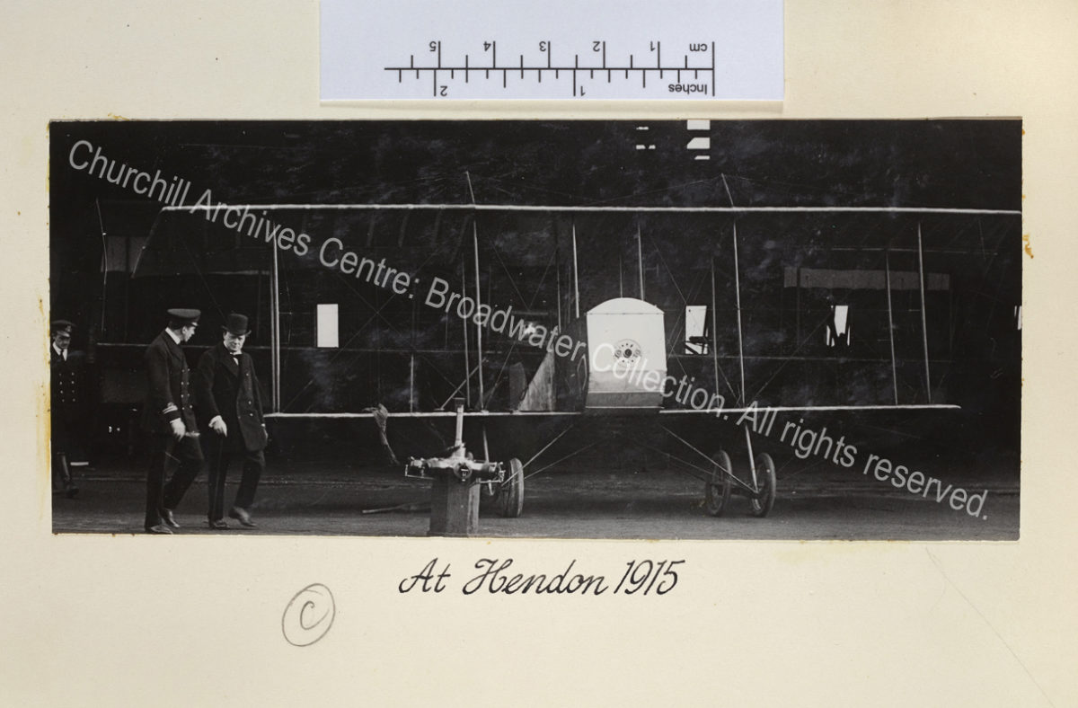 Photo of a bi-plane in a hangar. WSC walks in front of it