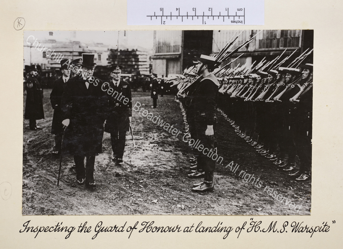 WSC wearing overcoat and top hat at the front of a small group inspecting two lines of sailors carrying bayonets.