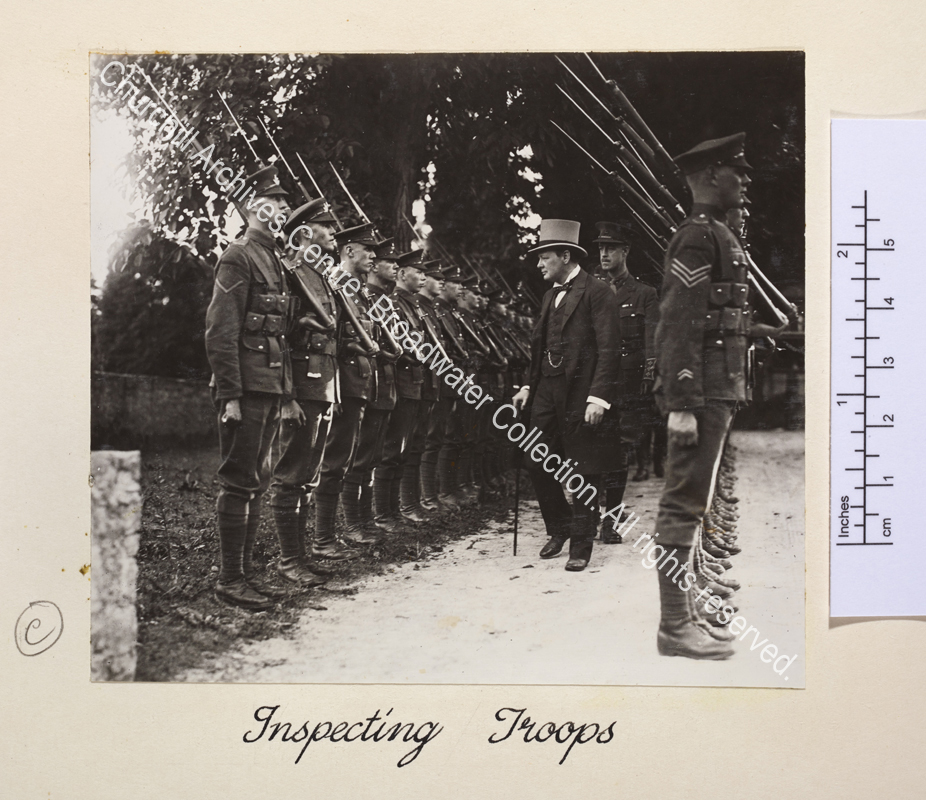 Photo shows WSC wearing a top hat and carrying a walking cane inspecting a line of British soldiers in Cologne
