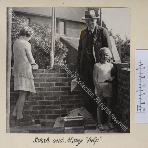 Photo of bricklaying at Chartwell. WSC stands holding a trowel with Sarah [Churchill