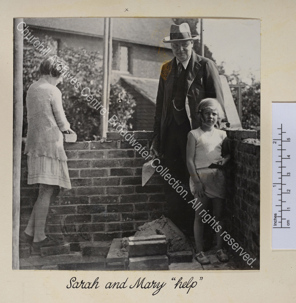 Photo of bricklaying at Chartwell. WSC stands holding a trowel with Sarah [Churchill