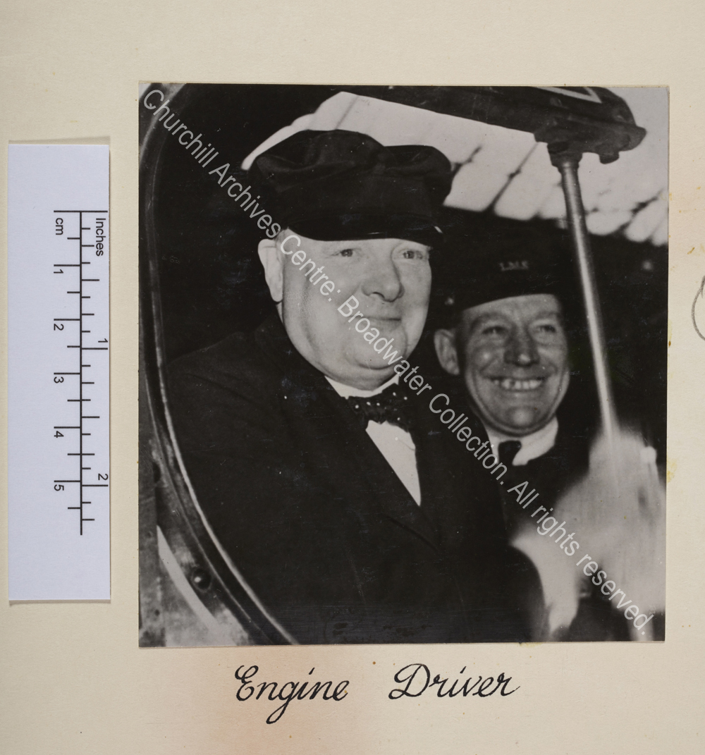Photo shows WSC smiling and wearing a cap. Just behind him is a man wearing a cap bearing the initials LMS [London
