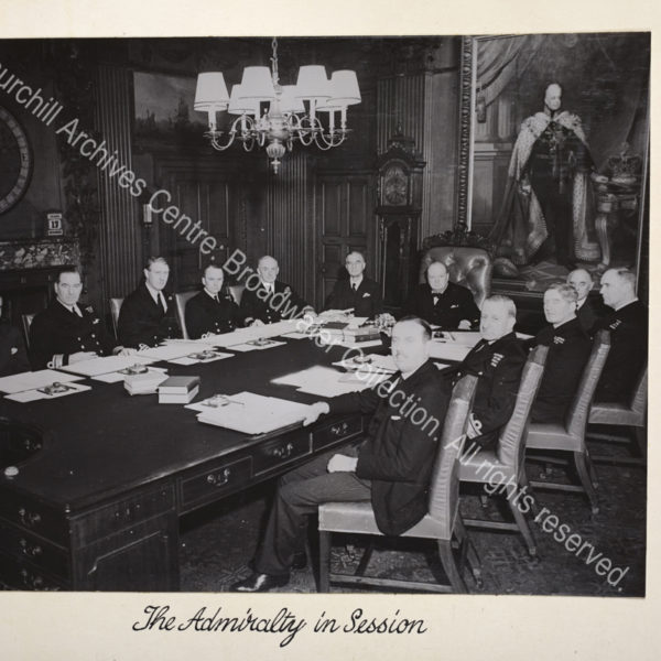Photo showing WSC at the head of a large meeting table. Admiralty staff and officers flank the table with meeting papers and blotters in front of them.