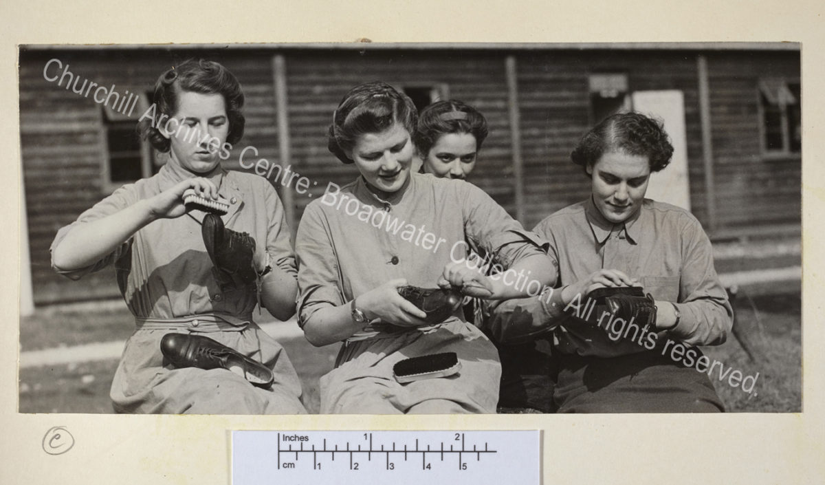 Photo shows Mary Churchill [later Mary Soames] with 3 other ATS [Auxiliary Territorial Services] recruits seated on the grass polishing lace up shoes.