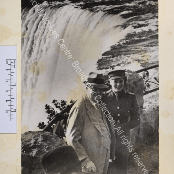 Photo of WSC wearing a pale suit and a hat standing next to Mary Churchill [later Mary Soames] with Niagara Falls behind them.