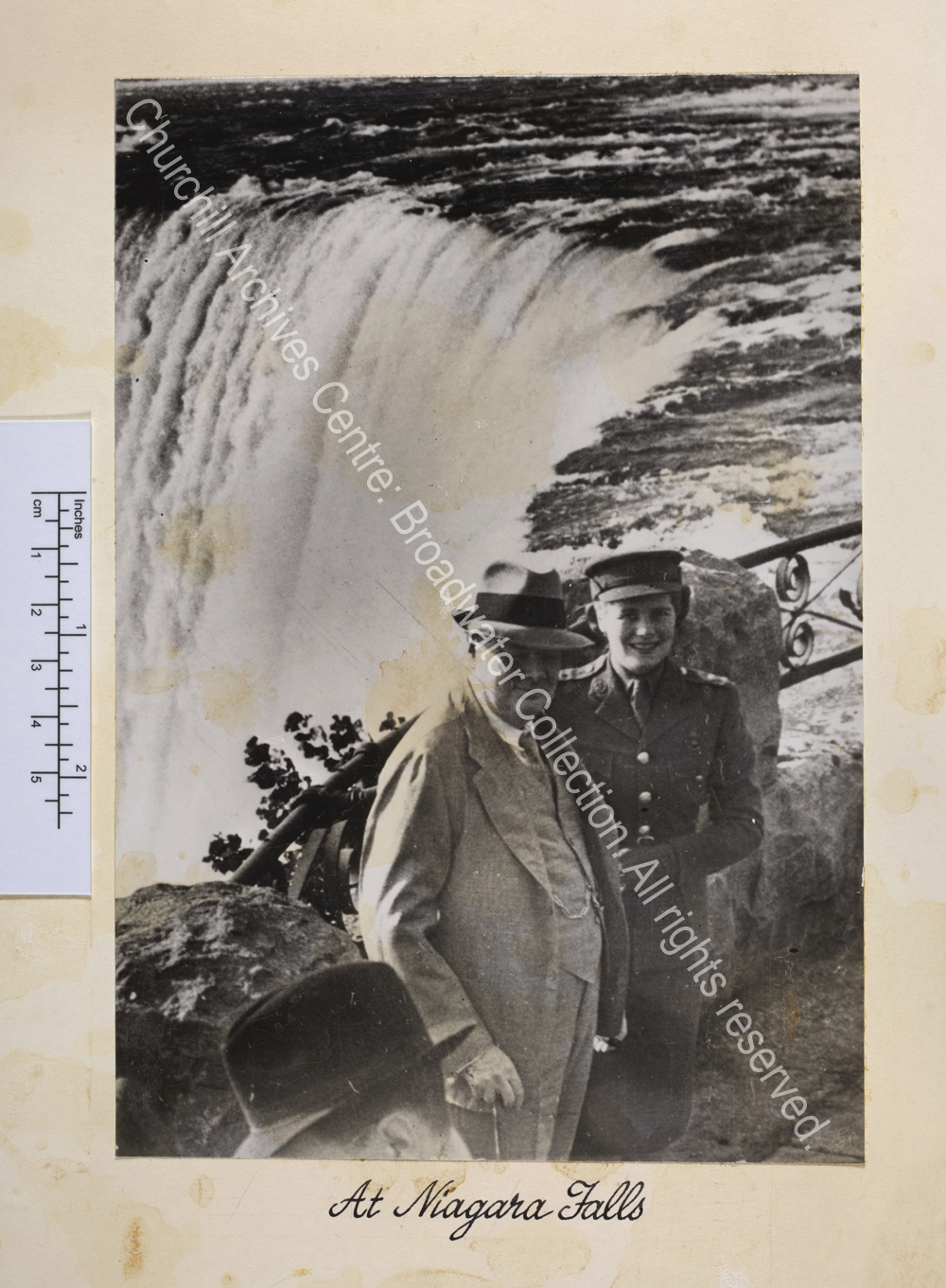 Photo of WSC wearing a pale suit and a hat standing next to Mary Churchill [later Mary Soames] with Niagara Falls behind them.