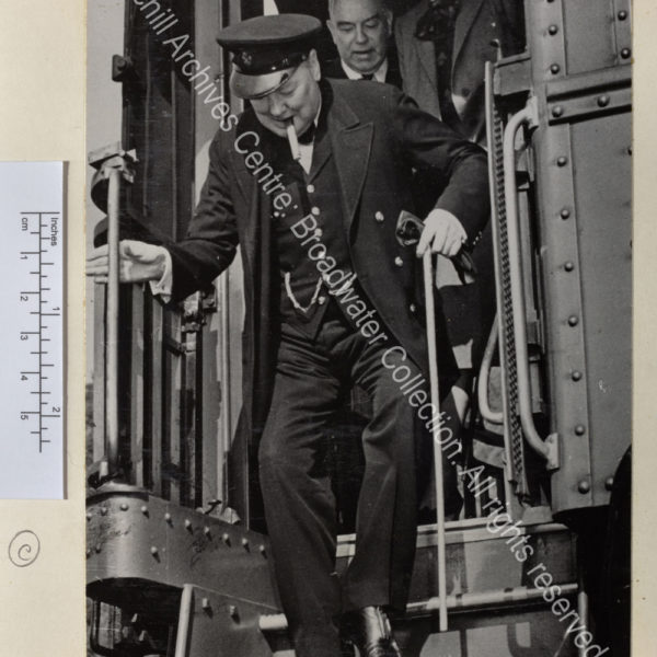 Photo shows WSC climbing down from his train arriving for the second Quebec Conference. He is wearing a peaked cap and has a cigar in his mouth. Behind him are CSC and Mackenzie King [Prime Minister of Canada]