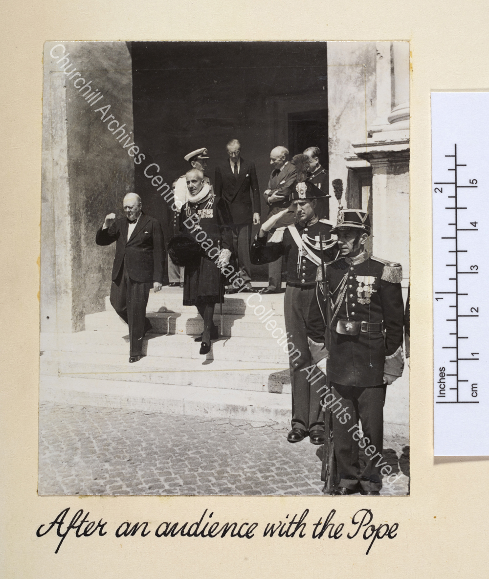 Photo shows WSC walking down exterior steps [?at the Vatican] with a uniformed Vatican official and soldiers.