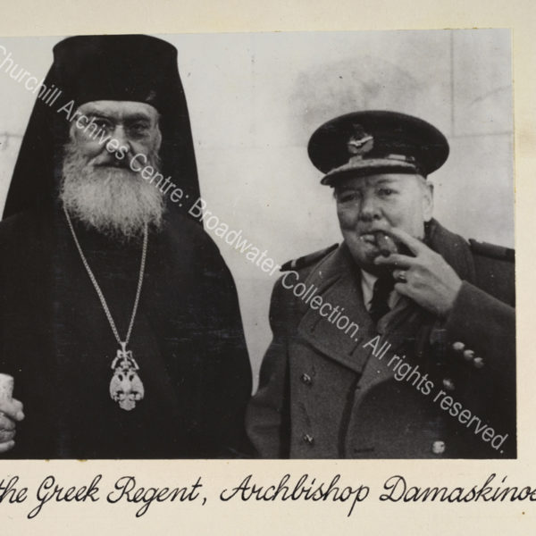 Head and shoulders photo of Archishop Damaskinos standing next to WSC. WSC is wearing uniform (including peaked cap and overcoat) and is smoking a cigar.