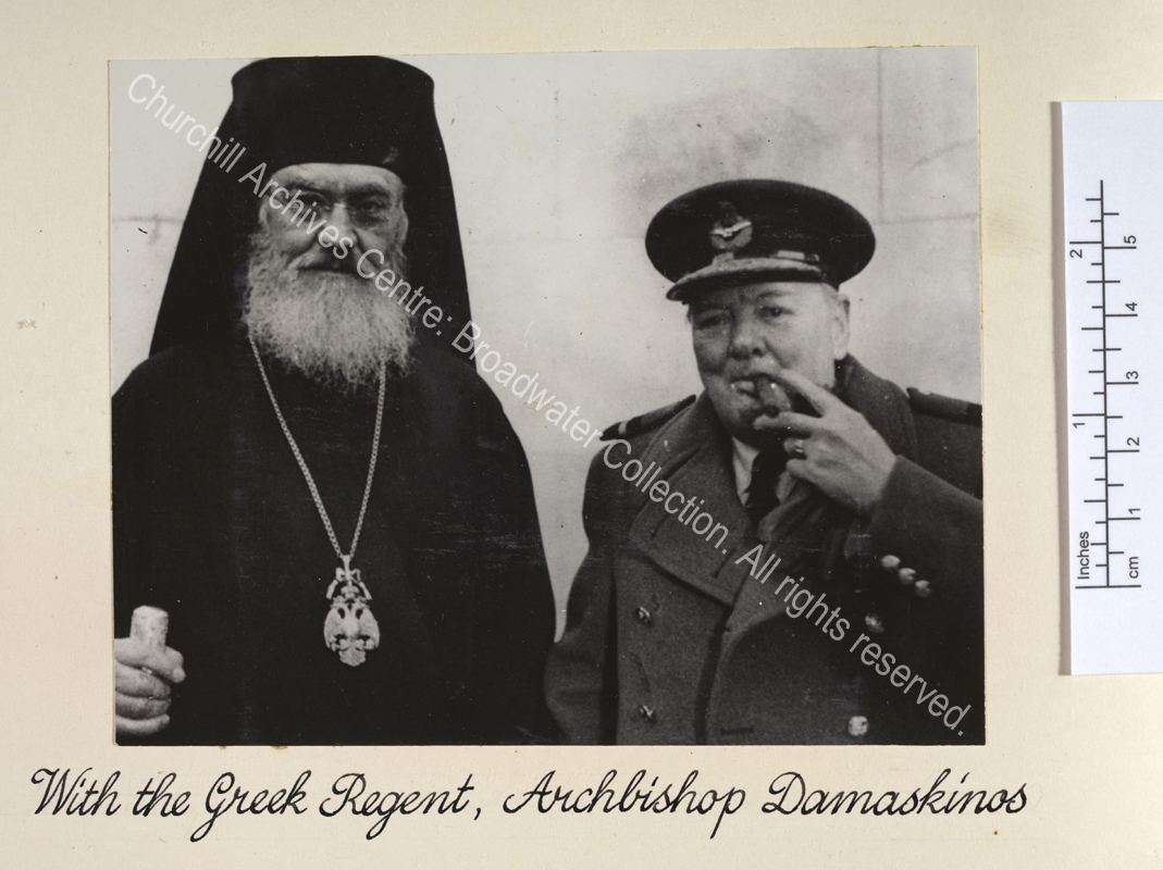 Head and shoulders photo of Archishop Damaskinos standing next to WSC. WSC is wearing uniform (including peaked cap and overcoat) and is smoking a cigar.