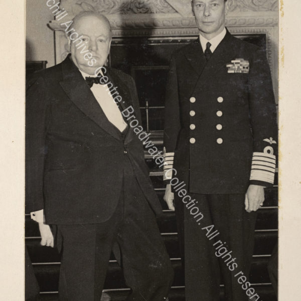 Photo shows WSC standing next to King George VI. The King is in uniform and WSC is wearing a dinner jacket and black tie.