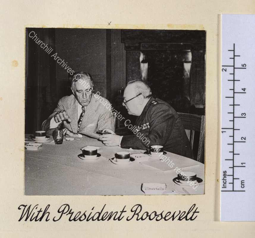 Photo shows WSC and President Roosevelt deep in conversation [at the Yalta conference]. They are sitting at a table on which there are empty coffee cups.