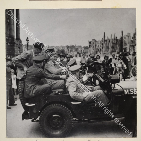 Photo shows WSC wearing a light suit and standing in a small motor boat with a town in the background. Among the passengers in the boat is a woman wearing a headscarf [?Mrs Margaret Nairn].