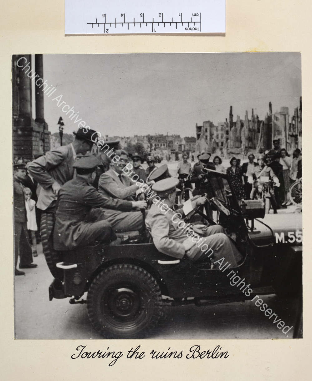 Photo shows WSC wearing a light suit and standing in a small motor boat with a town in the background. Among the passengers in the boat is a woman wearing a headscarf [?Mrs Margaret Nairn].