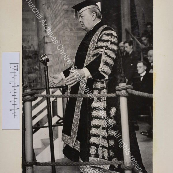 Photograph of WSC wearing his robes as Chancellor of Bristol University speaking at a microphone.