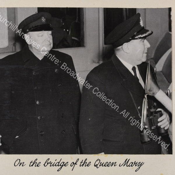 Photo shows WSC wearing an overcoat and peaked cap standing next to ?the captain.