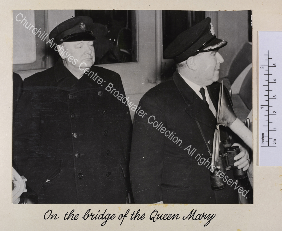 Photo shows WSC wearing an overcoat and peaked cap standing next to ?the captain.