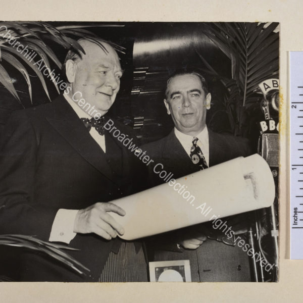 Photo shows WSC on the occasion of receiving the Gold Medal of the City of New York. He is standing in front of microphones smiling and holding a rolled paper. Next to him is Mayor William O'Dwyer.