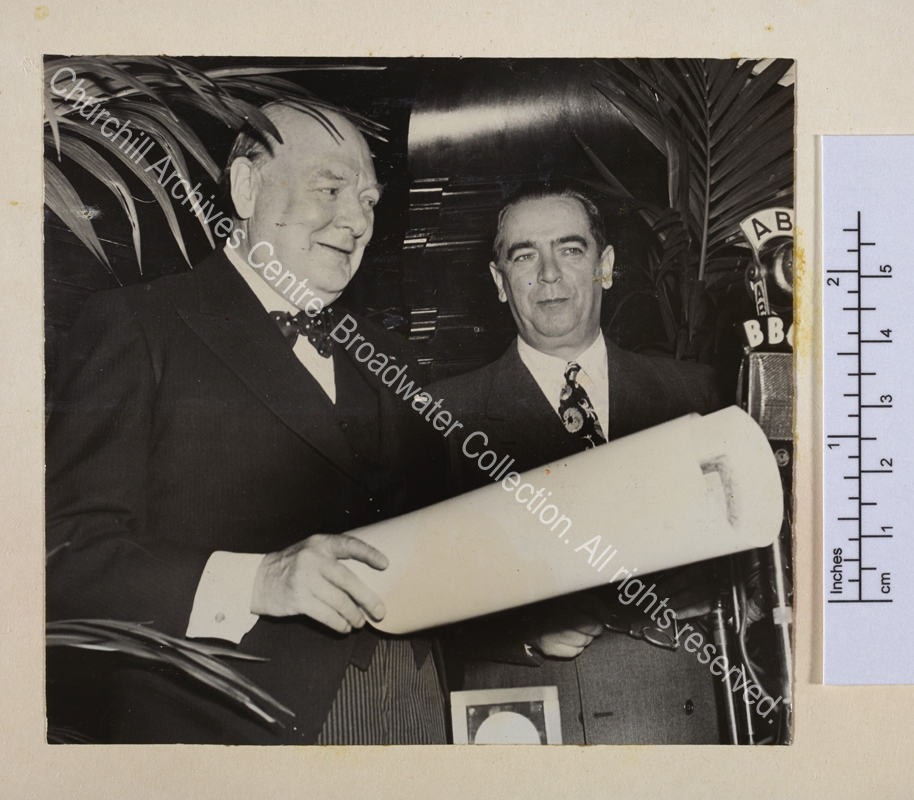 Photo shows WSC on the occasion of receiving the Gold Medal of the City of New York. He is standing in front of microphones smiling and holding a rolled paper. Next to him is Mayor William O'Dwyer.