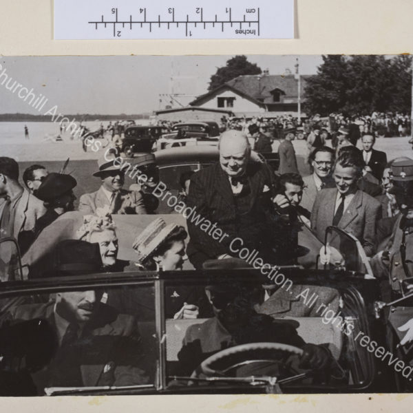 Photo shows WSC seating on the back of an open topped car. He is wearing a pinstriped suit and waistcoat. CSC and Mary Churchill [later Lady Soames] are in the back seat of the car