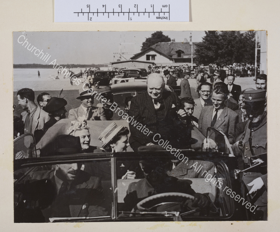 Photo shows WSC seating on the back of an open topped car. He is wearing a pinstriped suit and waistcoat. CSC and Mary Churchill [later Lady Soames] are in the back seat of the car