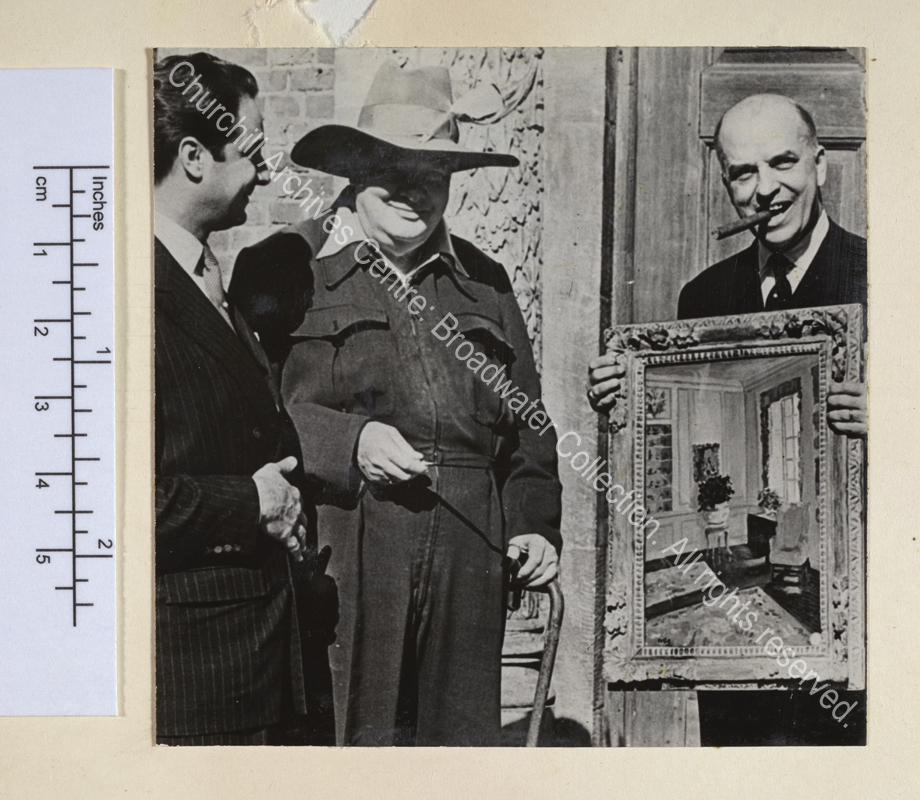 Photo shows WSC at the Chartwell entrance wearing a siren suit and a broad-brimmed sombrero hat with a feather in it. He is presenting his painting "The Blue Room