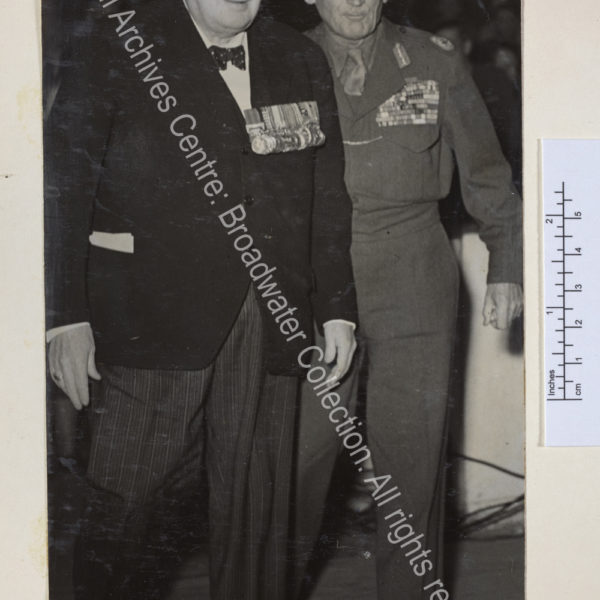 Full length photo of WSC and [1st Lord] Montgomery of Alamein. Both are wearing medals and WSC has speech notes visible in his pocket.