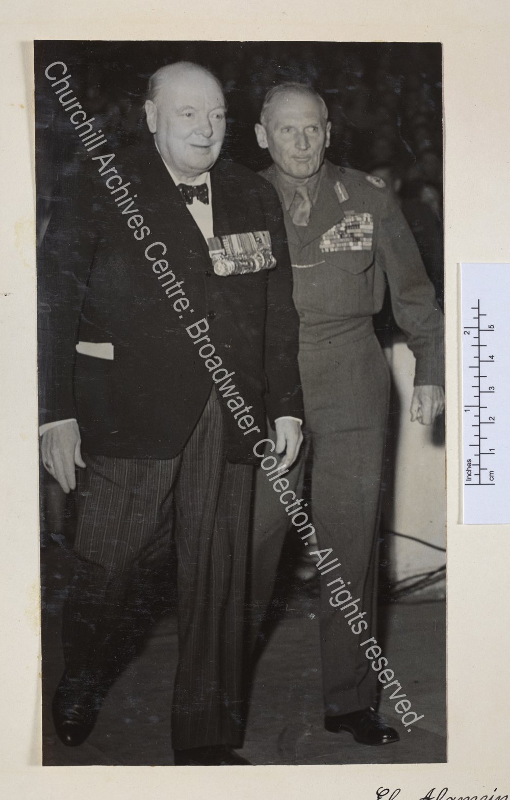Full length photo of WSC and [1st Lord] Montgomery of Alamein. Both are wearing medals and WSC has speech notes visible in his pocket.