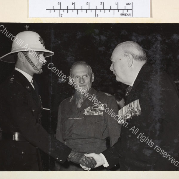 Photo of WSC shaking hands with an officer in uniform while [1st Lord] Montgomery of Alamein looks on. WSC and Montgomery are both wearing medals.