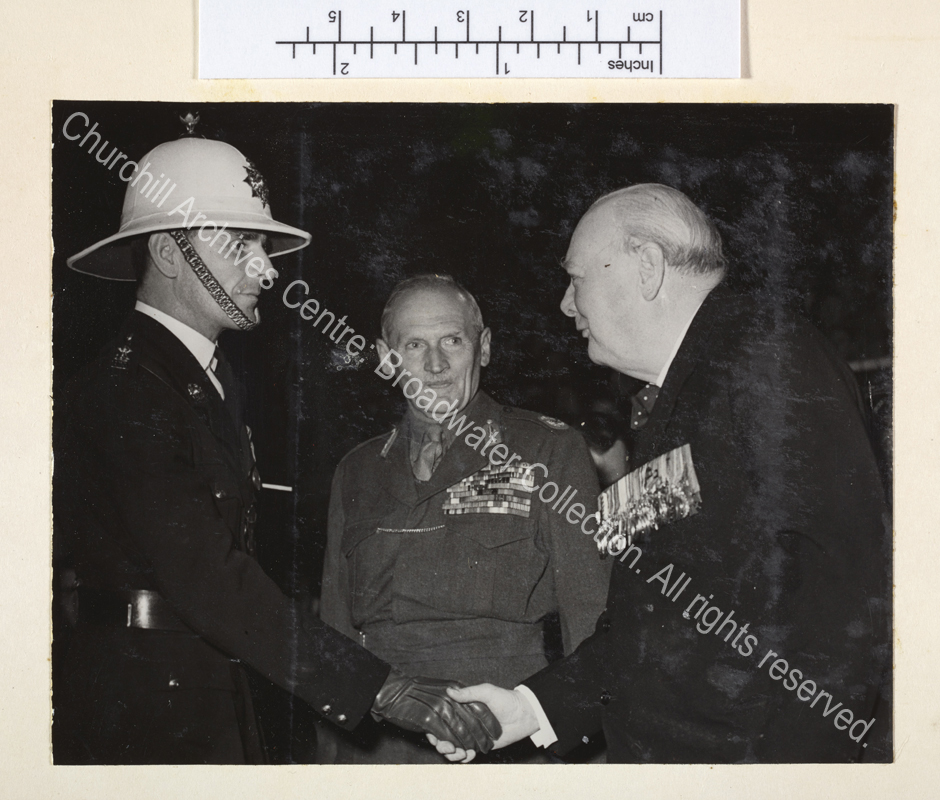 Photo of WSC shaking hands with an officer in uniform while [1st Lord] Montgomery of Alamein looks on. WSC and Montgomery are both wearing medals.