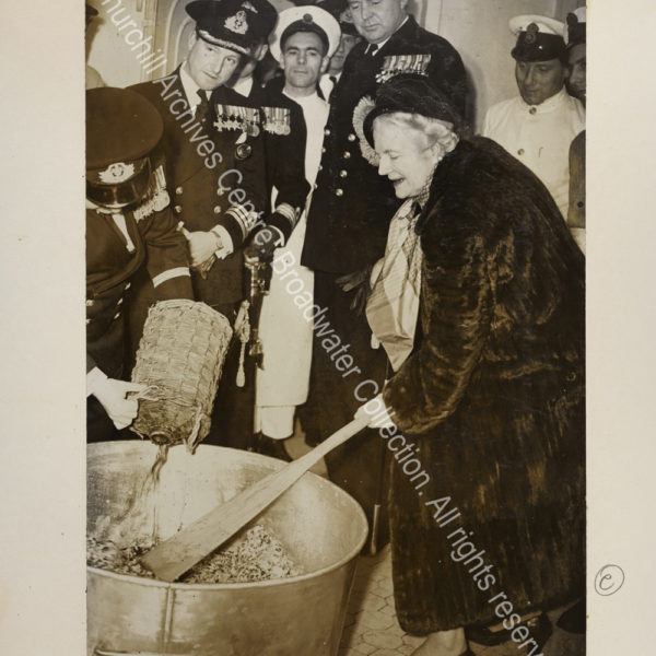 CSC is shown on board HMS Indomitable leaning over to use a large paddle to stir a huge pan. She is wearing a fur coat and is watched by naval officers and sailors.