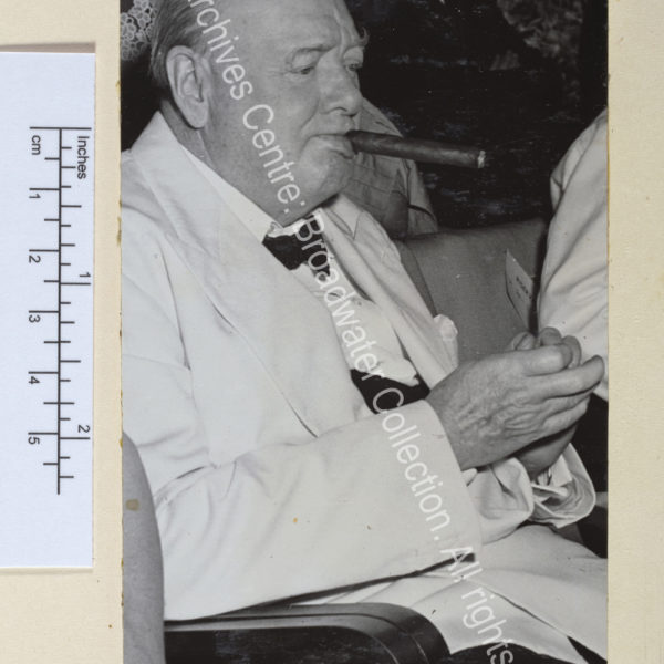 Photo shows WSC sitting and clapping. He is wearing a white jacket and black bow tie and has a cigar in his mouth.