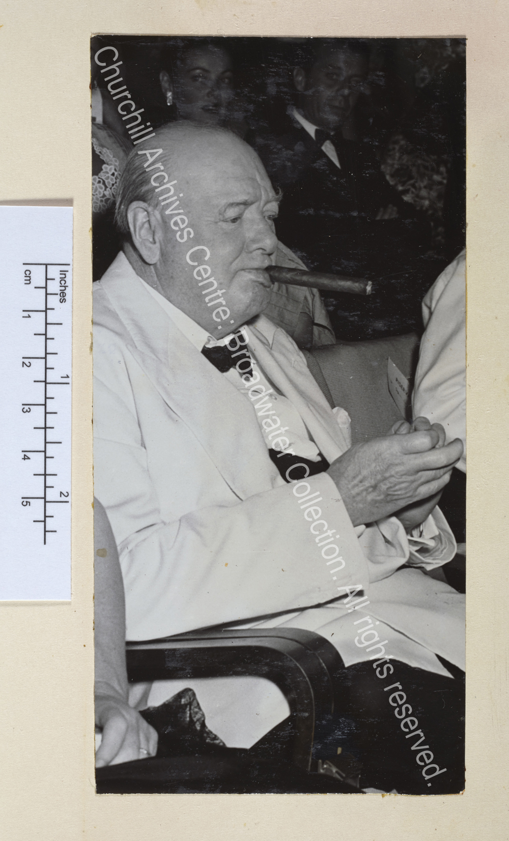 Photo shows WSC sitting and clapping. He is wearing a white jacket and black bow tie and has a cigar in his mouth.