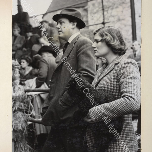 Exterior photo showing Christopher Soames and Mary Soames [earlier Mary Churchill] wearing a tweed jacket and carrying a dog [watching the auction of WSC's dairy herd].