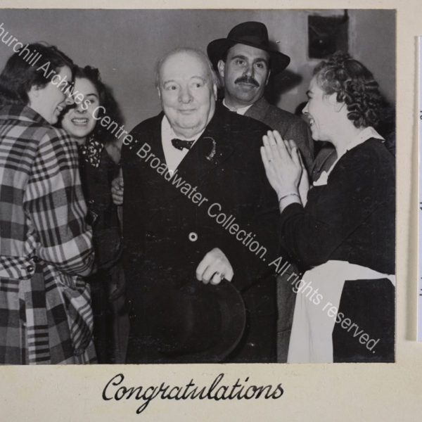 Photo shows WSC similing and surrounded by his staff. A maid in black and white uniform applauds.
