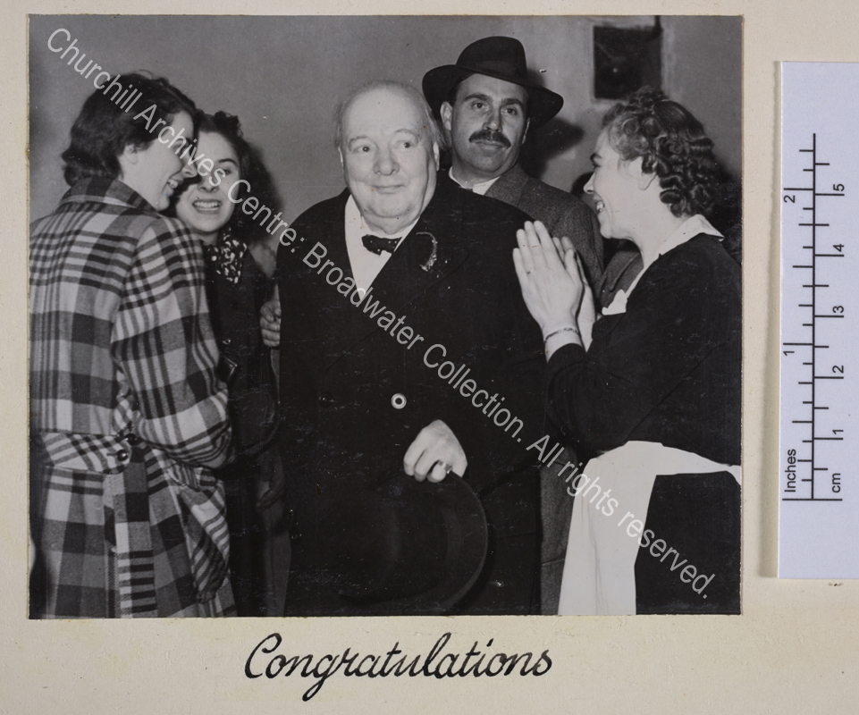 Photo shows WSC similing and surrounded by his staff. A maid in black and white uniform applauds.