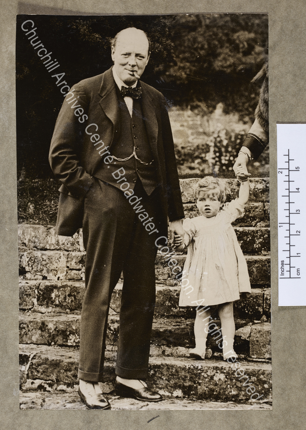 Photograph of WSC standing on the steps of the garden at Chartwell [Kent] holding the hand of Mary Churchill [later Mary Soames] as a toddler.  WSC