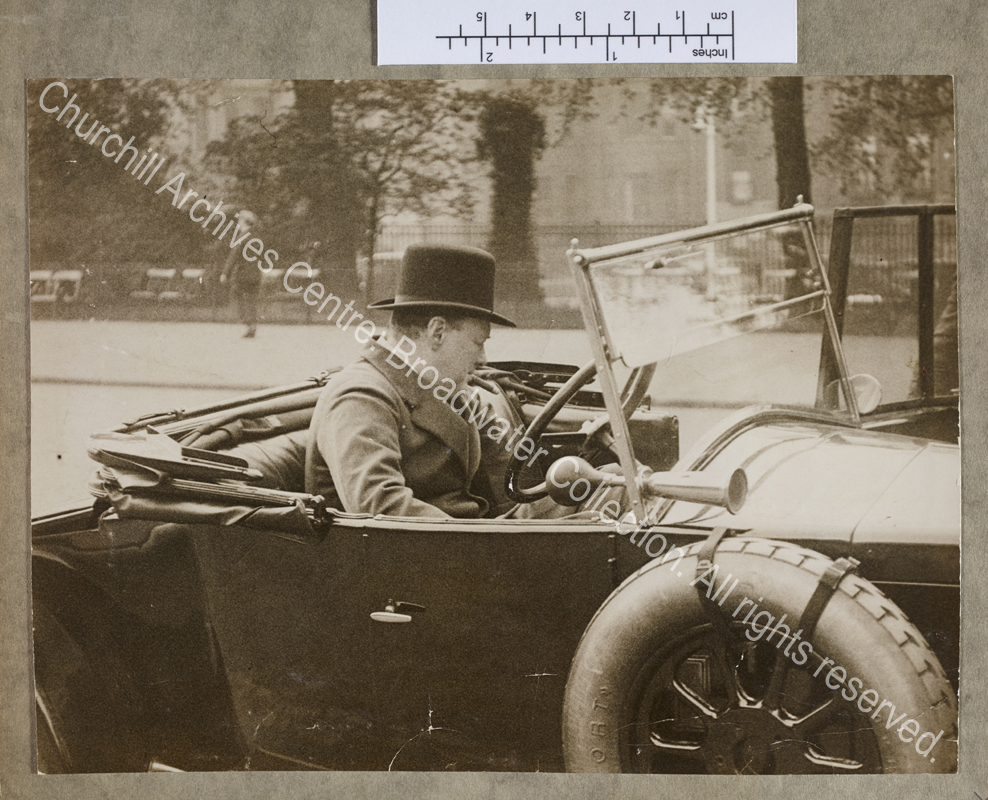 Photograph of WSC [Chancellor of the Exchequer] sitting in his open-topped car [? a Wolseley] by the side of the road in Westminster [London].  WSC is turned away from the camera