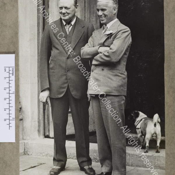 Full length photograph of WSC standing with Chaplin in the doorway at Chartwell [Kent].  They are both smiling and looking to the left