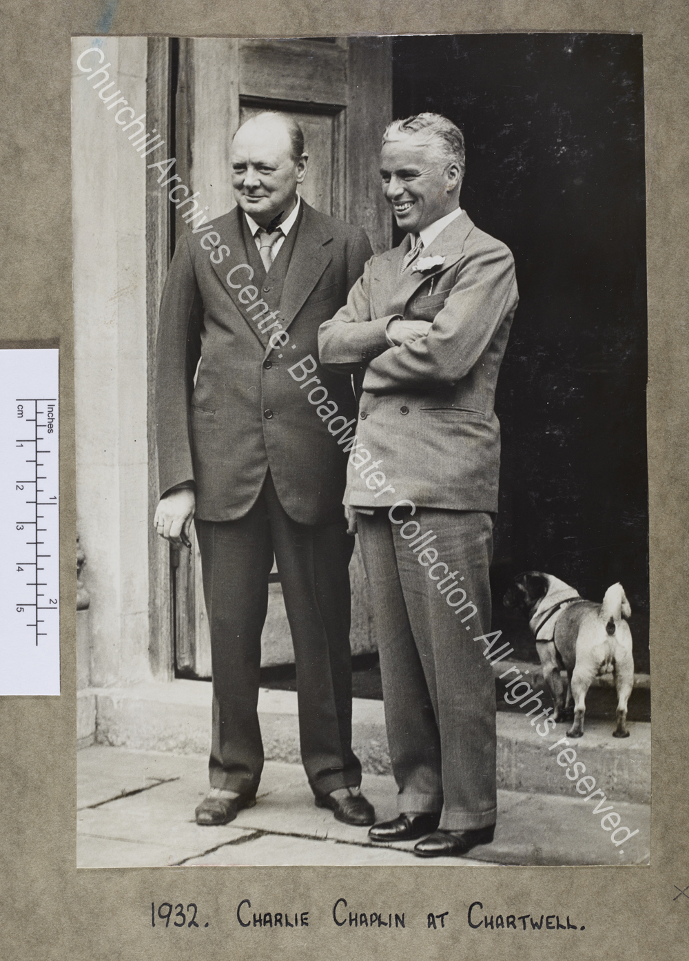 Full length photograph of WSC standing with Chaplin in the doorway at Chartwell [Kent].  They are both smiling and looking to the left